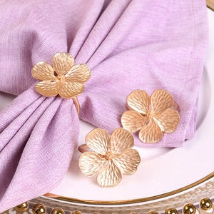 Close-up of matte gold flower napkin rings on a white plate with purple napkins