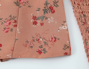 Détail du tissu à fleurs rose orangé avec poignets élastiques et coutures précises