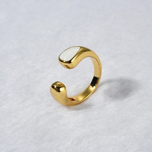 Close-up of golden adjustable ring with white teardrop enamel detail on soft background