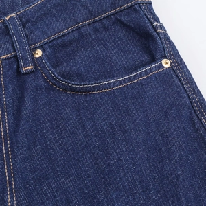 Détail macro du jean bleu foncé montrant les rivets métalliques et les surpiqûres jaunes