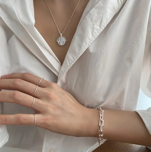 Close-up of minimalist 925 silver embossed pendant necklace and rings on model