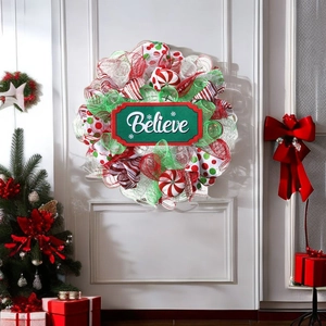 Christmas wreath with Believe sign on white door next to a tree and gift boxes