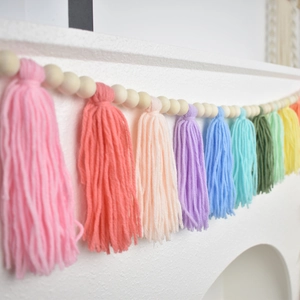 Detail of colorful yarn tassels and wooden beads hanging on a white mantel for home decor