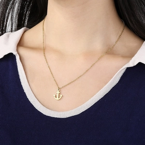 Detail of a golden anchor pendant necklace worn on a model's neck with fine chain style