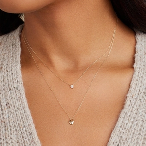 Close-up of golden double-layer necklace with heart and lock pendants on a model