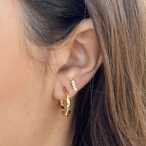 Close-up of golden twisted hoop earrings and rectangular zircon studs on model