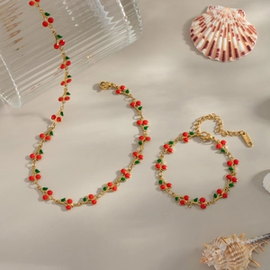 18K gold plated stainless steel cherry necklace and bracelet set on beach themed backdrop
