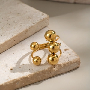 Gold stainless steel geometric open ring featuring polished spheres on stone background