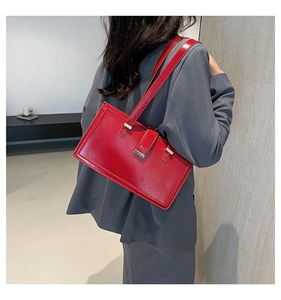 Close-up of bright red leather rectangular shoulder bag worn with a grey-blue blazer