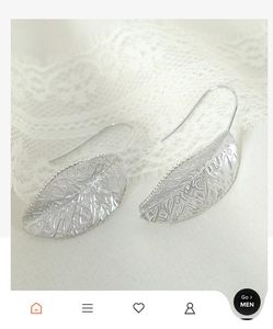 Macro shot of silver leaf drop earrings with intricate filigree texture on lace cloth