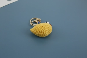 Macro shot of handmade yellow crochet chicken pendant with red comb and golden metal keychain