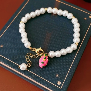 Detail of dragon fruit charm and white pearls on a gold-plated bracelet on vintage book