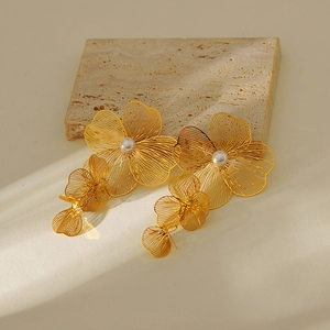 Detailed close-up of gold flower tassel earrings with pearls on natural stone background