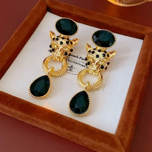 Detailed view of vintage gold tiger head earrings with black drop pendants in a jewelry box
