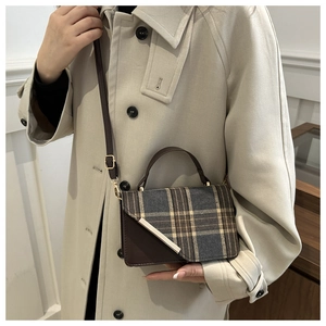 Close-up of a vintage plaid crossbody bag worn over a trench coat for size reference