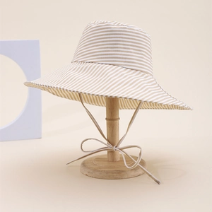 Beige wide brim striped sun hat with adjustable strap on a minimalist wooden stand