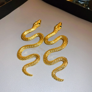 Detail shot of golden snake stud earrings featuring green gemstone eyes and scales