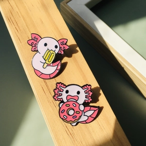Lot de pins en émail axolotl rose avec glace et donut sur une surface en bois
