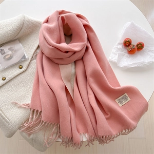 Pink cashmere-feel knit scarf with fringe and brand label on a stylish white setup