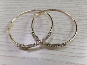 Detail of large gold hoop earrings featuring clear rhinestone accents on wood background