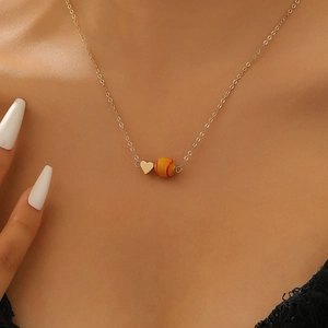 Detail einer minimalistischen Goldkette mit Herz- und Softball-Anhänger am Halsausschnitt