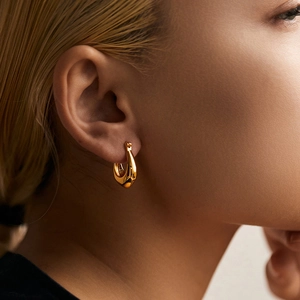 Close-up of a minimalist gold-plated U-shaped hoop earring worn on the earlobe