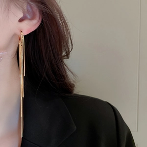 Macro view of long gold-plated metal tassel earrings on a model with black suit