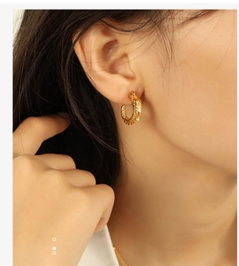 Close-up of golden C-shaped hoop earrings with hammered texture worn on ear
