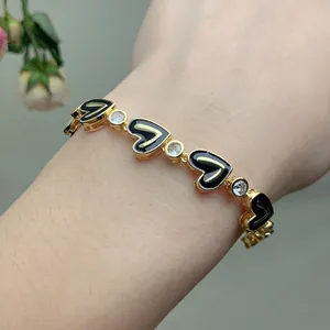 Close-up of gold chain bracelet with black enamel hearts and clear zircon stones on wrist