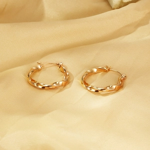 Gros plan de boucles d'oreilles torsadées en acier titane plaqué or 18K sur soie champagne