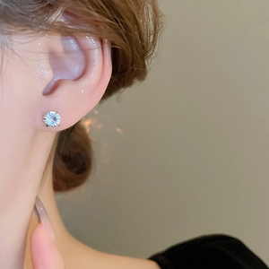 Close-up of a sparkling round zircon stud earring in silver setting worn on earlobe