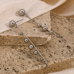 Detail view of silver stainless steel bead tassel earrings on a natural rock surface