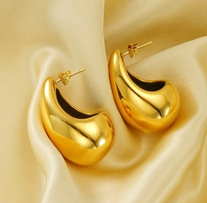 Macro detail of gold chunky teardrop earrings placed on smooth golden silk fabric