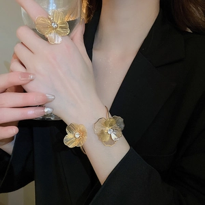 Detail of gold brushed flower ring and bracelet set worn by a model on black background