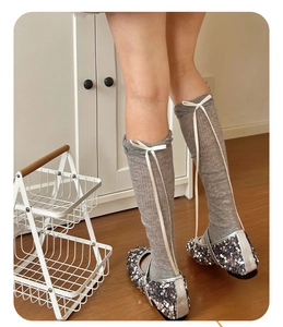 Detail of ballet style grey knee high socks with white ribbons and silver sequin shoes