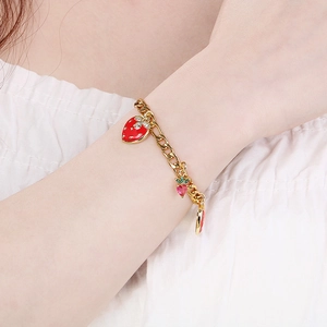 Detailed macro view of a gold strawberry charm bracelet with pink heart crystals and green leaves