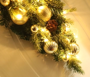 Detail der Weihnachts-Türdekoration mit goldenen Kugeln, Zapfen und LED-Lichterkette