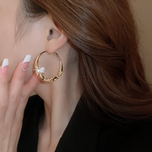 Close-up of large golden twisted hoop earrings with diamond accents worn by a model