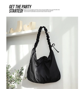 Detail of minimalist black nylon shoulder bag with drawstring straps and pleated texture