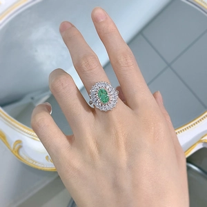 Close-up of a silver halo ring featuring an oval green gemstone and white diamonds
