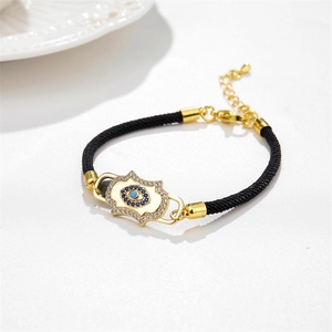 Close-up of black braided bracelet with gold Hamsa Hand and blue Evil Eye charm