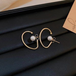 Detail view of elegant C-shaped golden metal earrings with a white pearl on leather