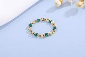 Dettaglio dell'anello a catena in oro 18K con sei perle verdi su sfondo blu