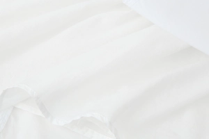 Detailed macro view of the white cotton dress fabric showing texture and hemline stitching