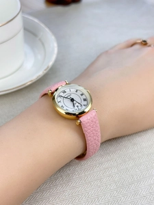 Close-up of golden Roman numeral watch with pink leather strap worn on wrist