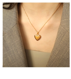 Detailed view of a gold heart pendant necklace styled with a vintage plaid blazer jacket
