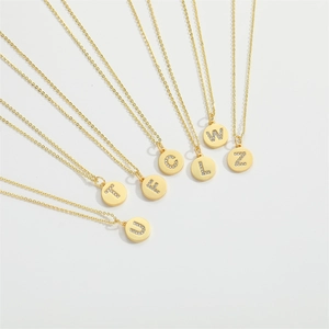 Group of seven gold necklaces with round crystal-encrusted letter pendants on white background