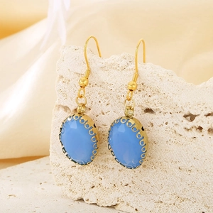 Detail of light blue oval glass earrings with gold hooks on a natural stone base