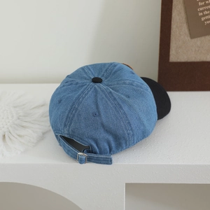 Detail of adjustable metal buckle and bear patch on blue denim baseball cap
