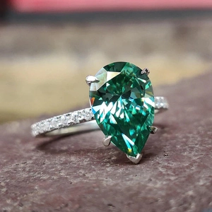 Vue latérale macro d'une bague en argent à pierre verte taille poire et petits diamants